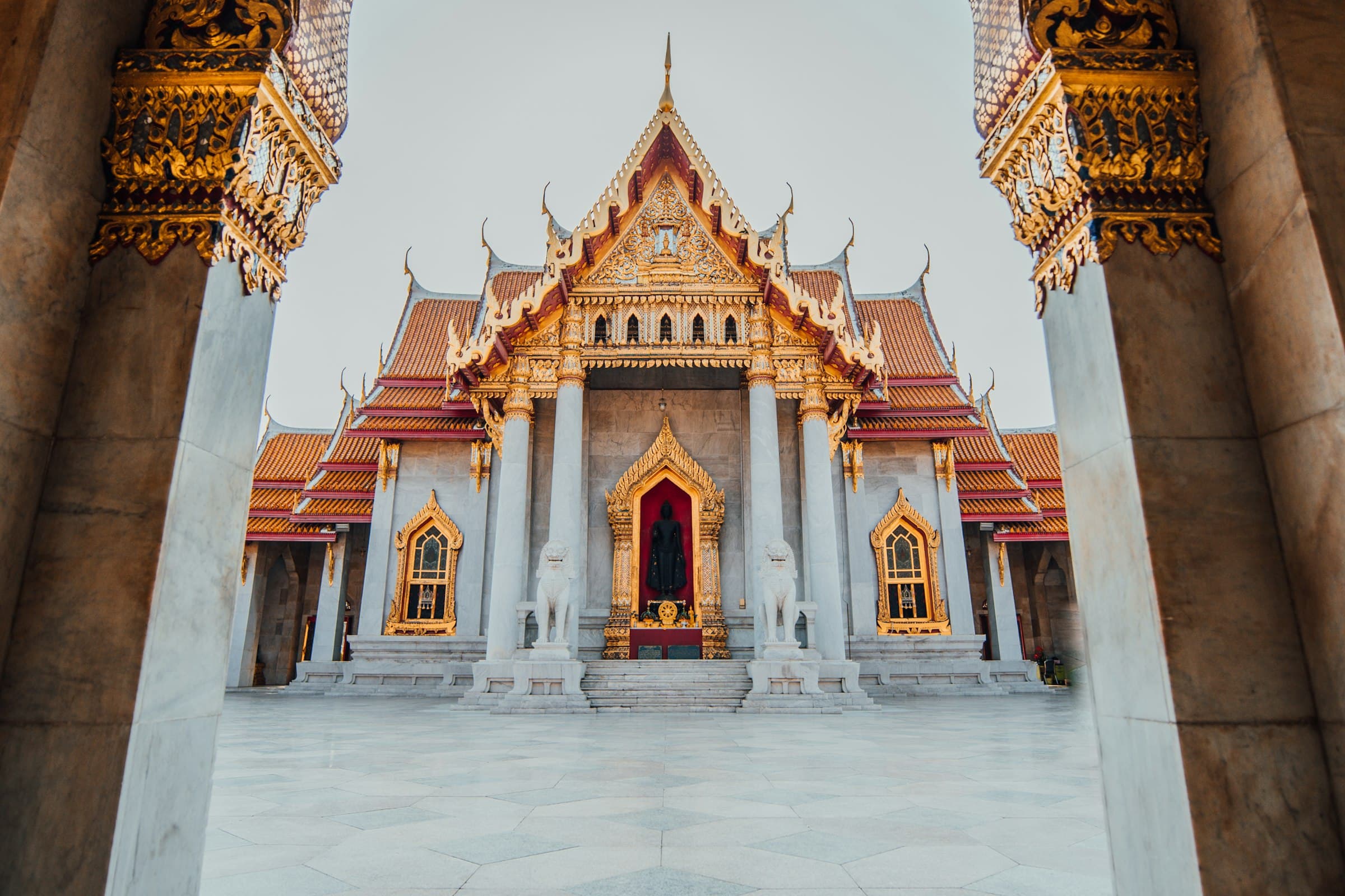 Wat Benchamabophit in Bangkok, de marmertempel, gezien tussen twee marmeren zuilen door in het ochtendlicht.