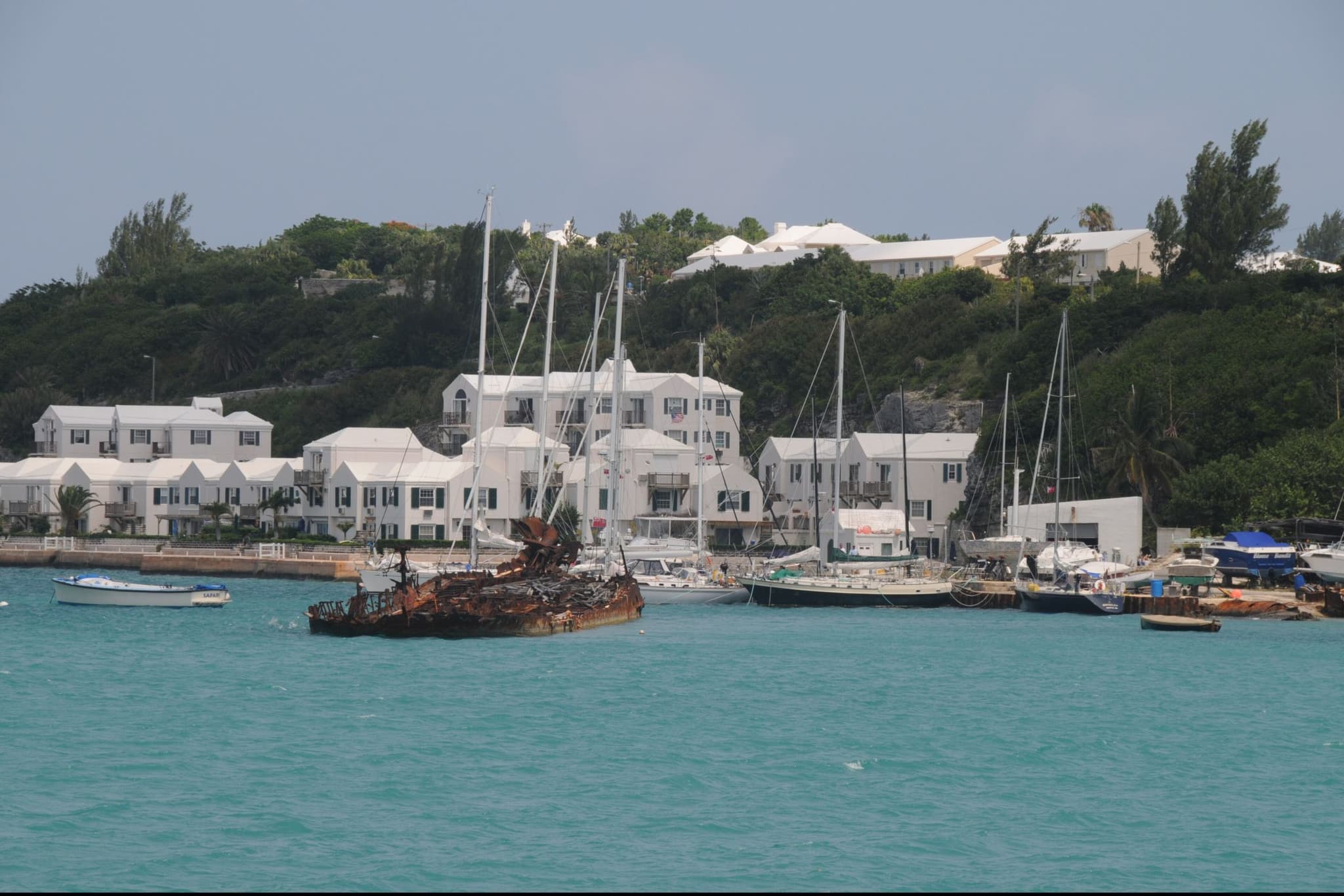 De haven van St. George's op Bermuda: turquoise water met zeilboten, en daarachter witte huizen met witte daken tegen een groene heuvel.