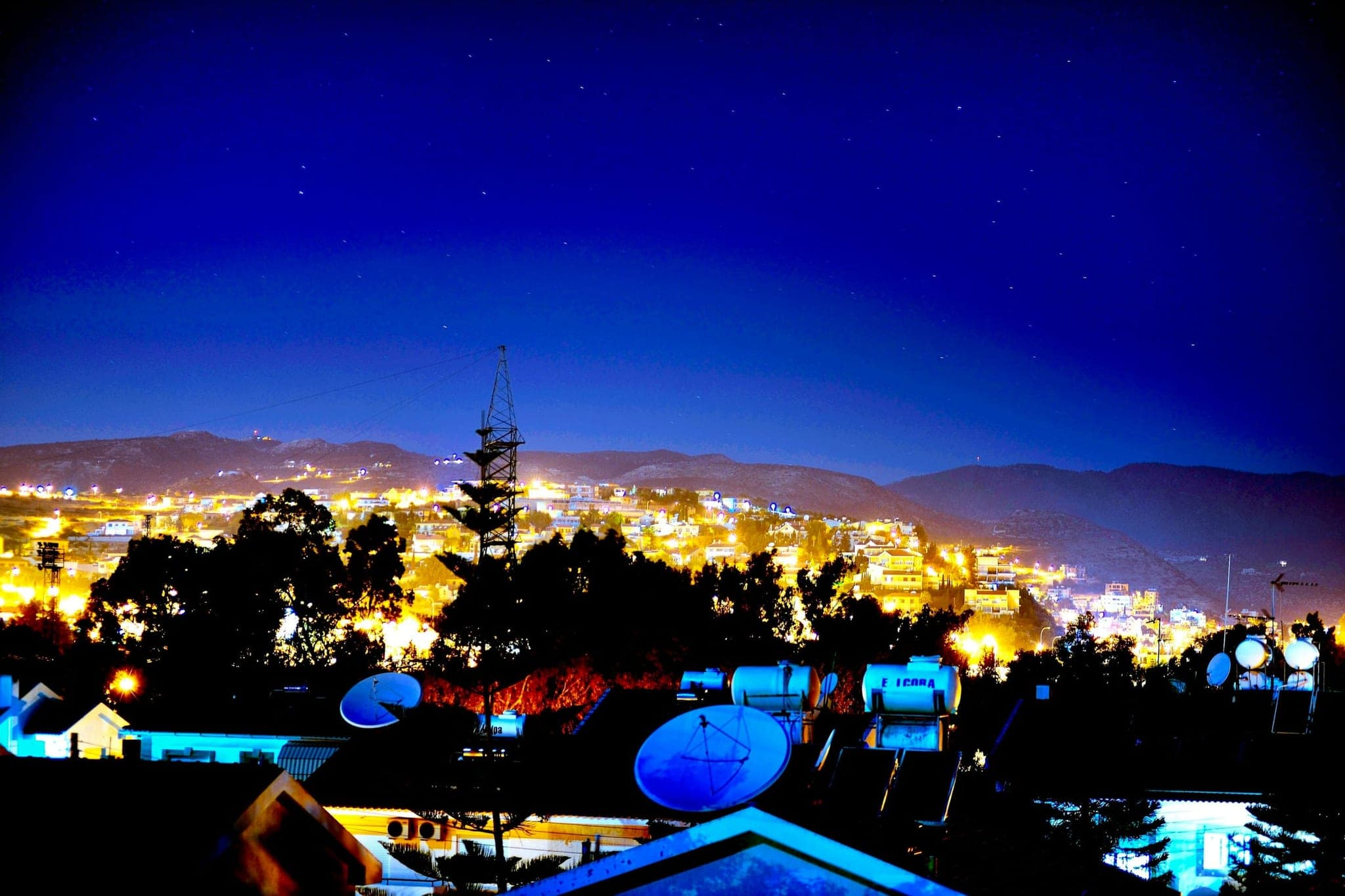 Limassol at night from a rooftop: the lights of the city under a deep blue sky, with the mountains behind.