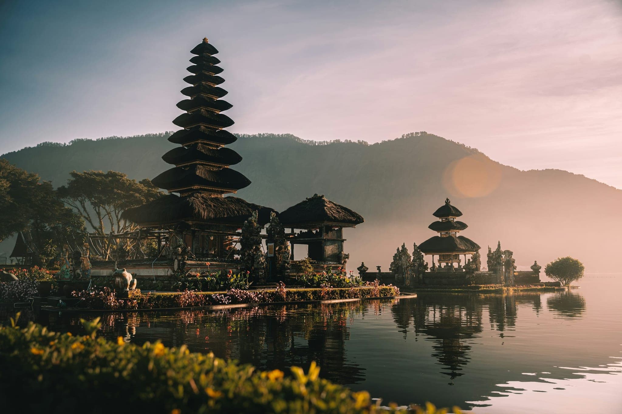 A Balinese water temple with tiered roofs on a lake in the morning mist, with the mountains behind.