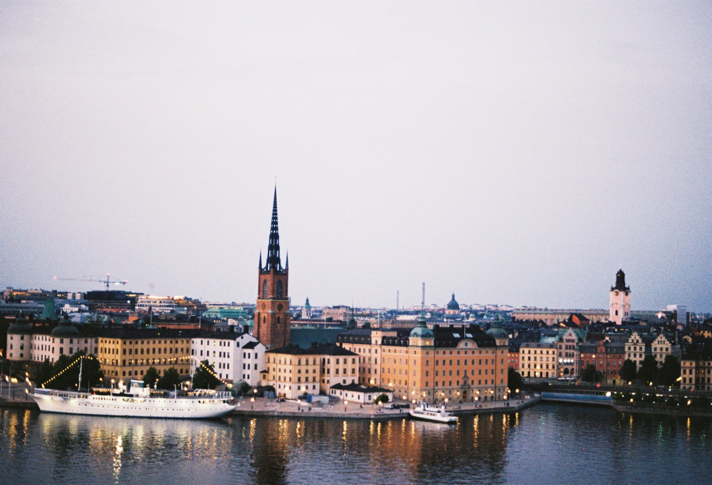 De skyline van Stockholm bij schemer, gezien over het water, met de stad zacht verlicht onder een kalme avondlucht.