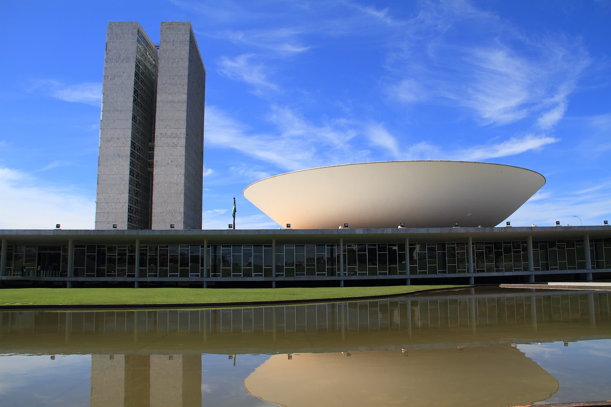 Het Congresso Nacional in Brasília: de twee witte torens naast de omgekeerde koepel van de Kamer, weerspiegeld in de vijver ervoor, onder een strakblauwe lucht.