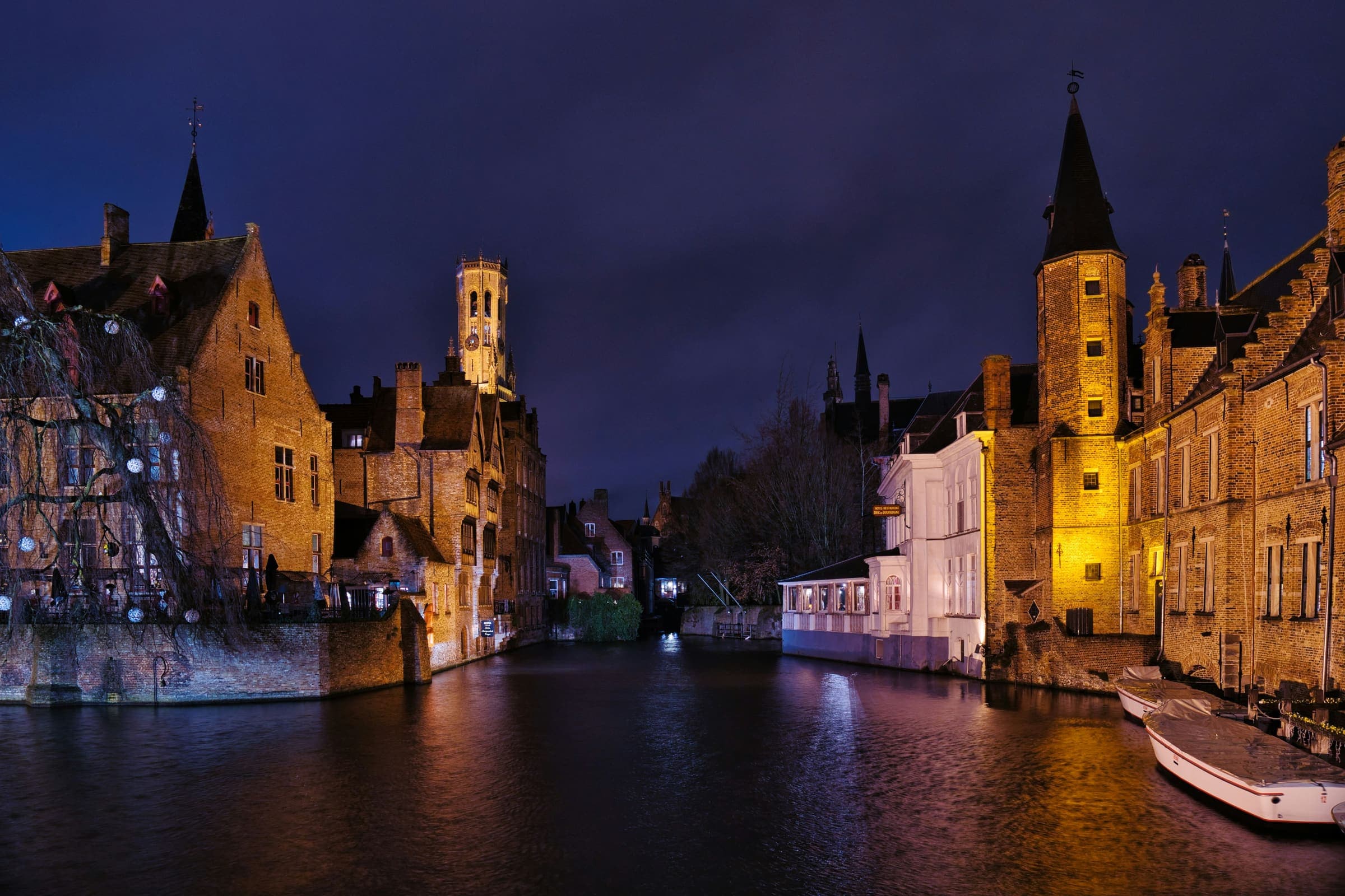 De Rozenhoedkaai in Brugge in het blauwe uur, met het verlichte Belfort weerspiegeld in het stille water van de reie.