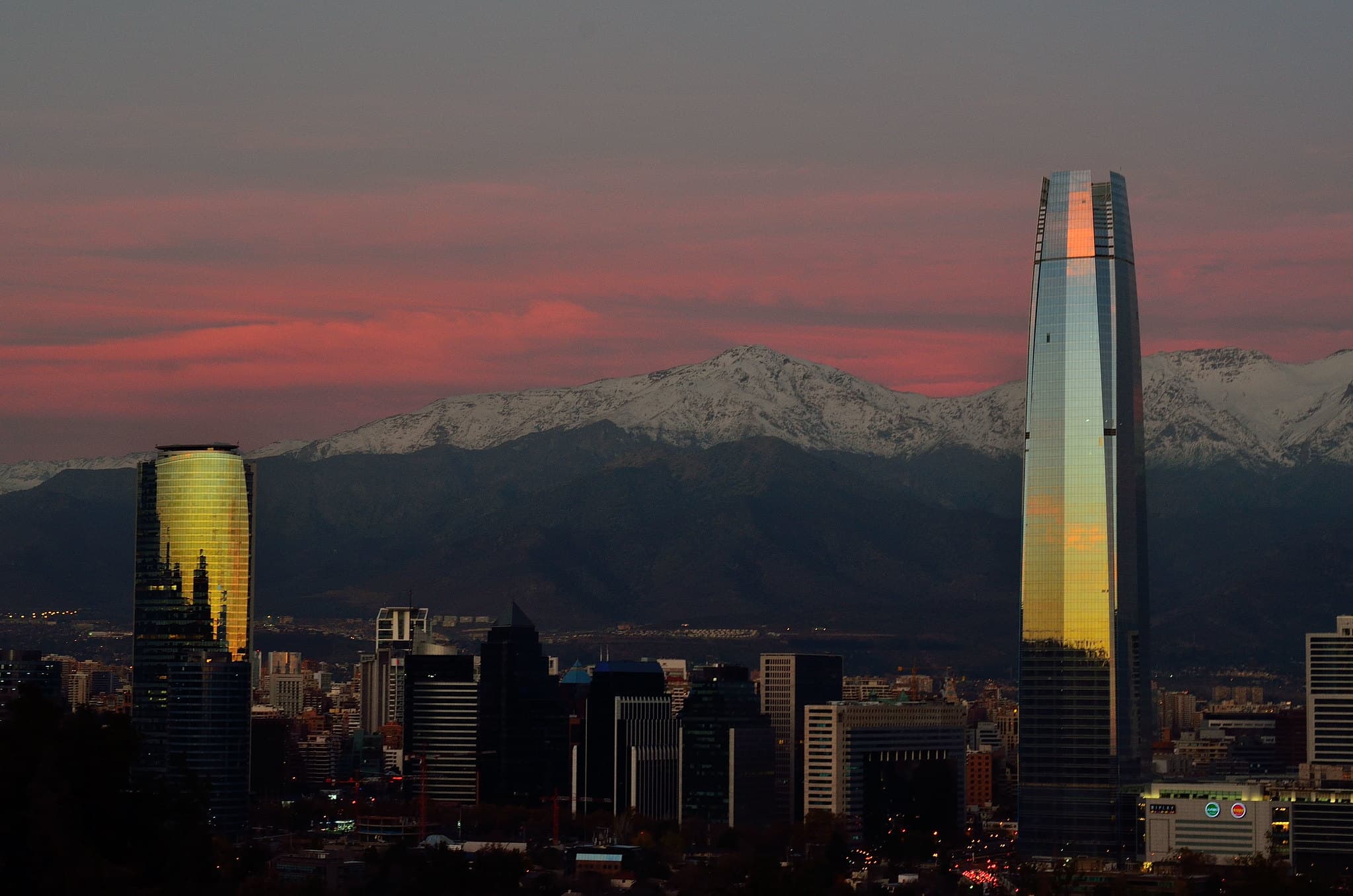 Santiago at dusk: the Gran Torre Santiago and the towers of the business district against the snow-capped Andes, under a pink sky.