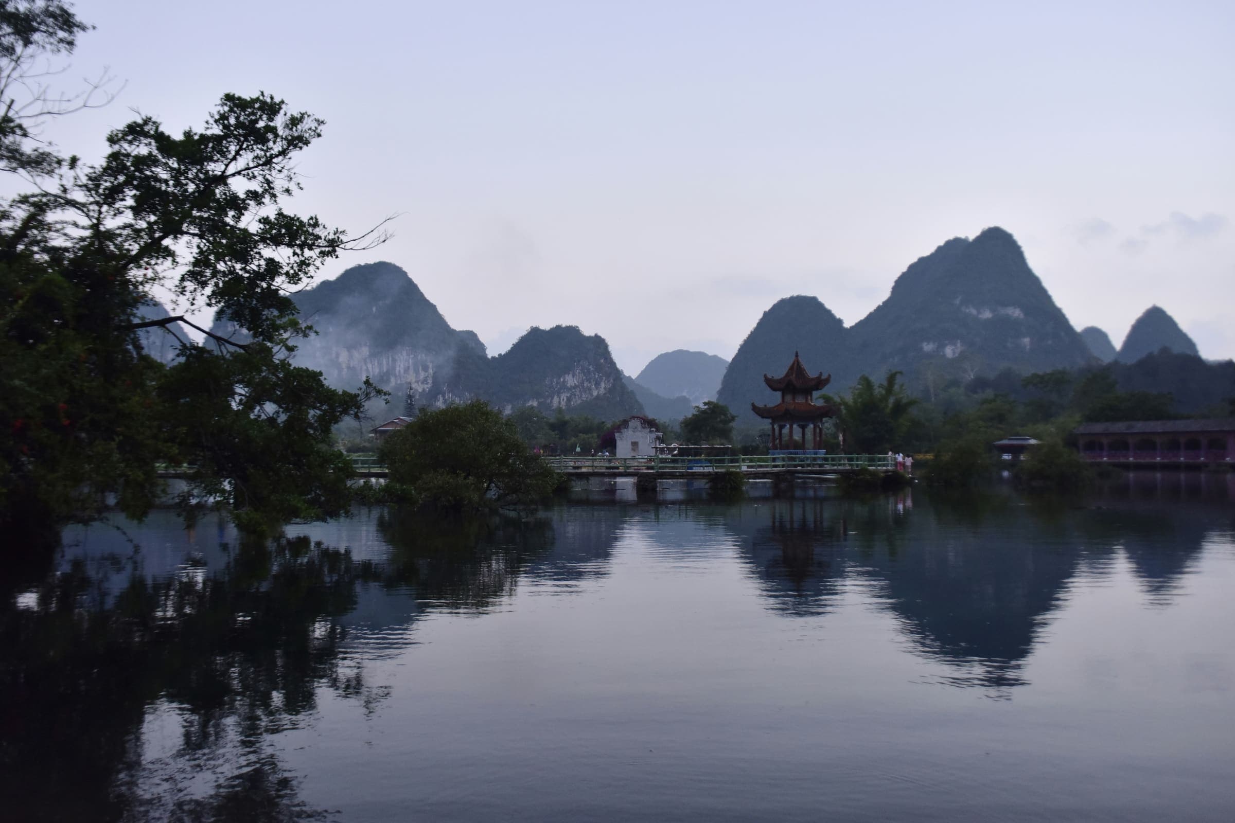 Karstbergen en een Chinees paviljoen gespiegeld in het stille water van de E'quan-bron bij Jingxi, in de blauwe avondschemering.