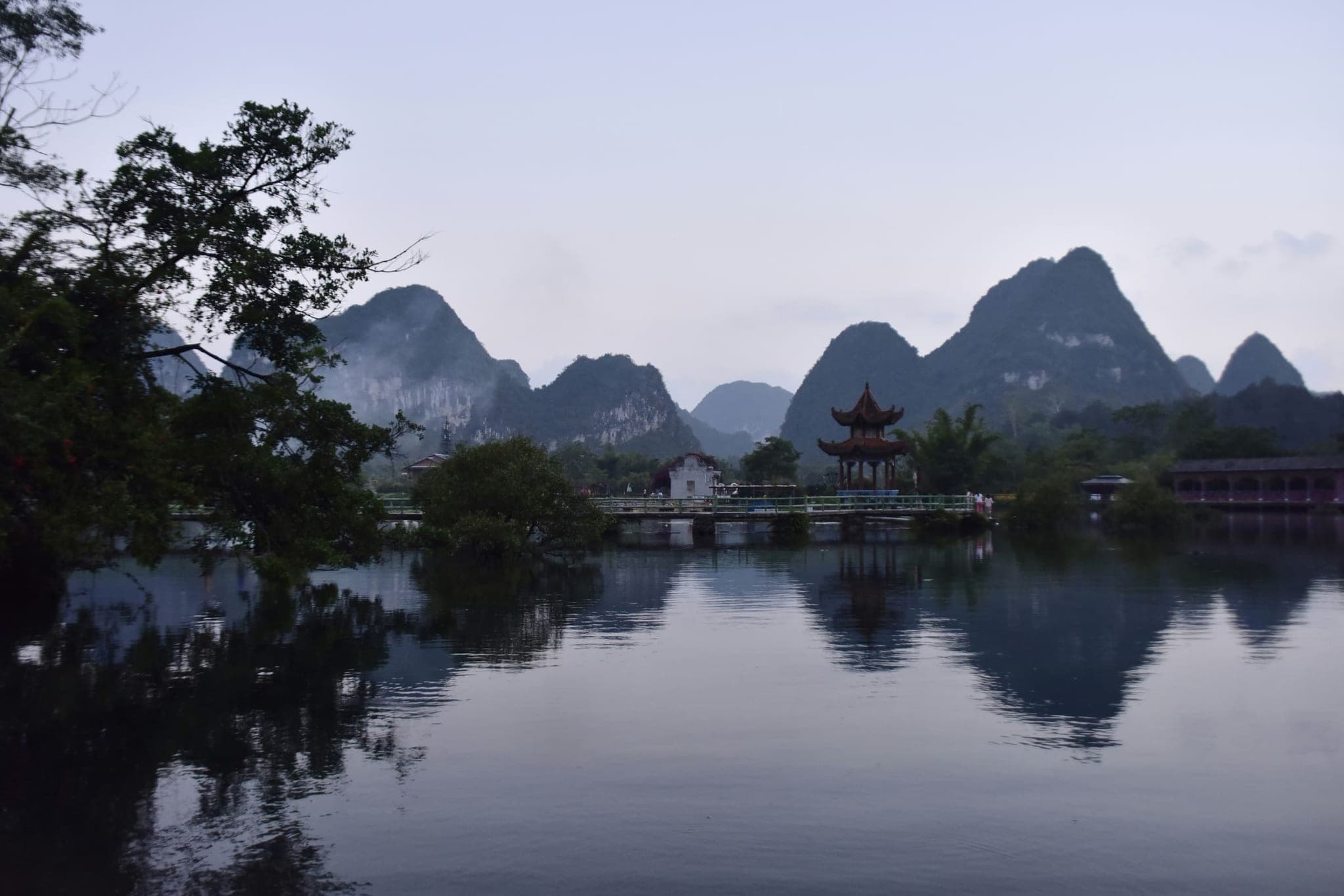 Karst mountains and a Chinese pavilion mirrored in the still water of the E'quan spring near Jingxi, in the blue evening dusk.