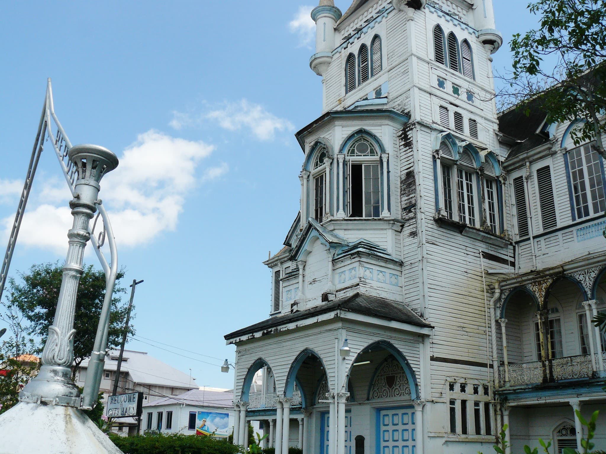 The white wooden City Hall of Georgetown, with its neo-Gothic tower, ornate balconies and a wrought-iron lamp post in the foreground, under a blue sky.