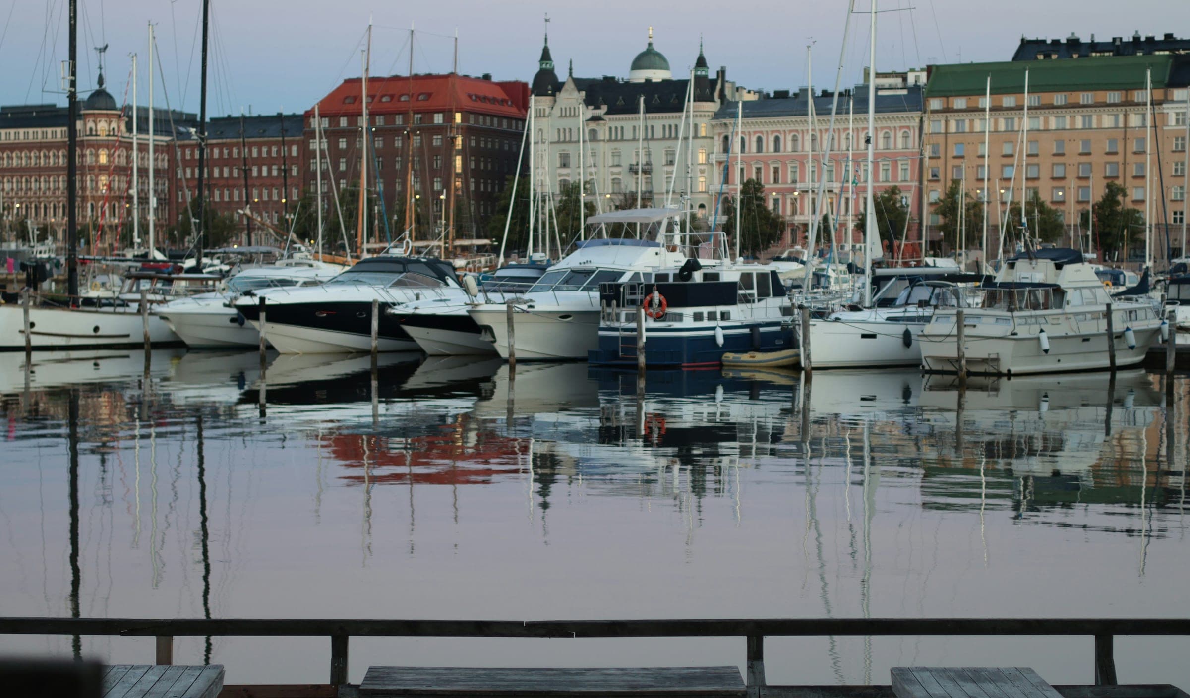 De jachthaven van Helsinki in het blauwe uur, met de gevels van de kade en de koepel van de kathedraal weerspiegeld in het stille water.