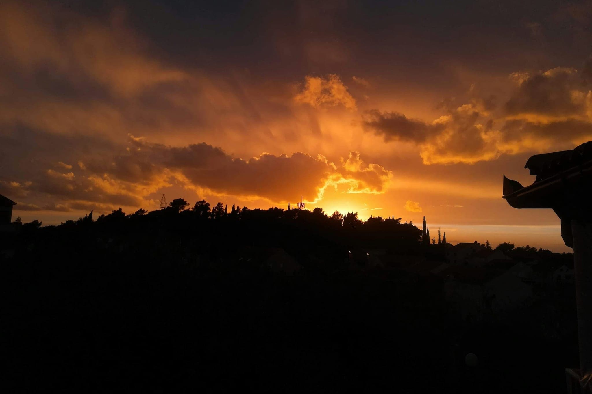 Sunset above Dubrovnik: the sun breaks through the clouds above a dark ridge with cypresses.