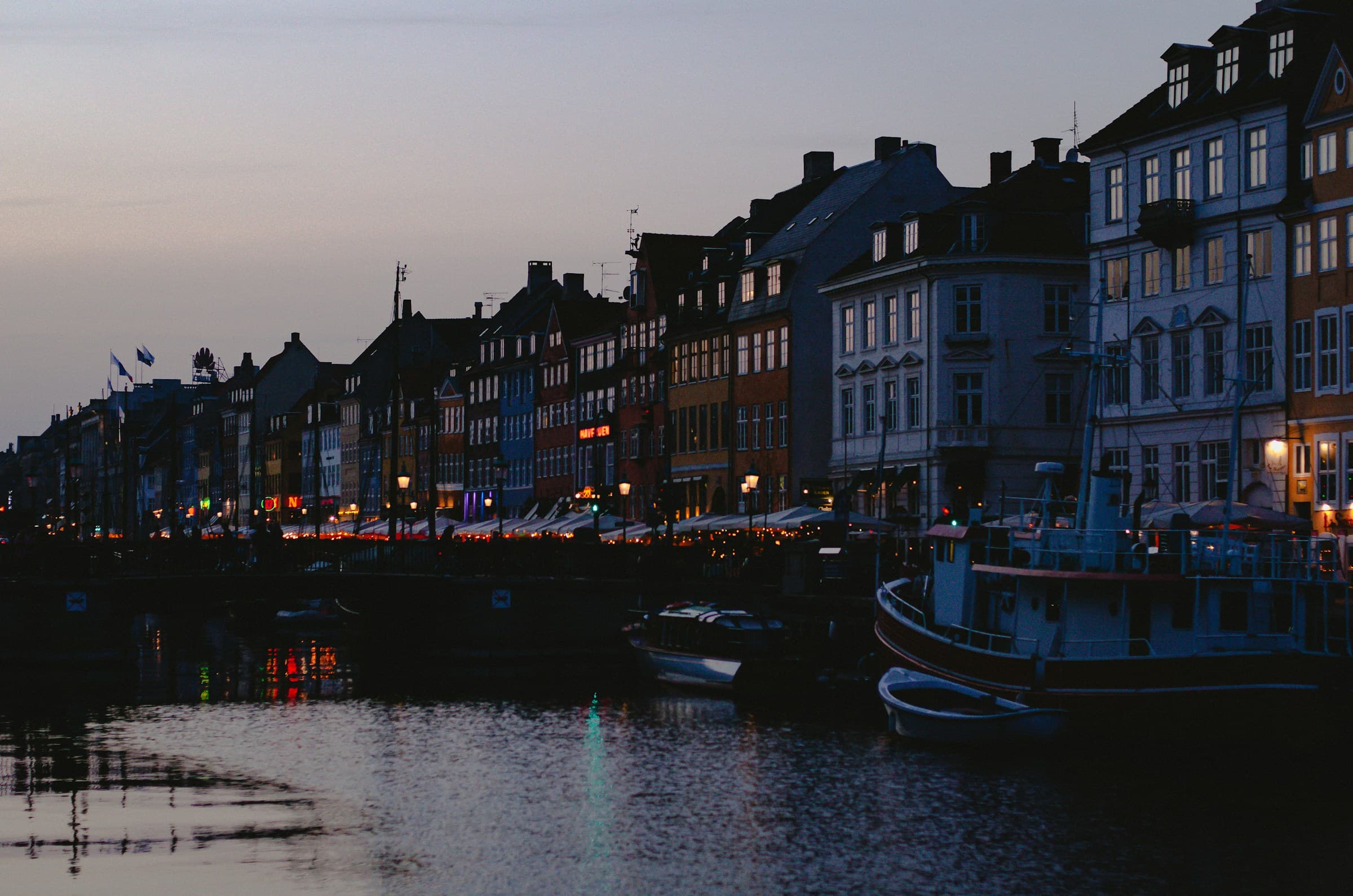 De haven van Nyhavn in Kopenhagen bij schemer: de gekleurde gevels en aangemeerde boten, gespiegeld in donker water.