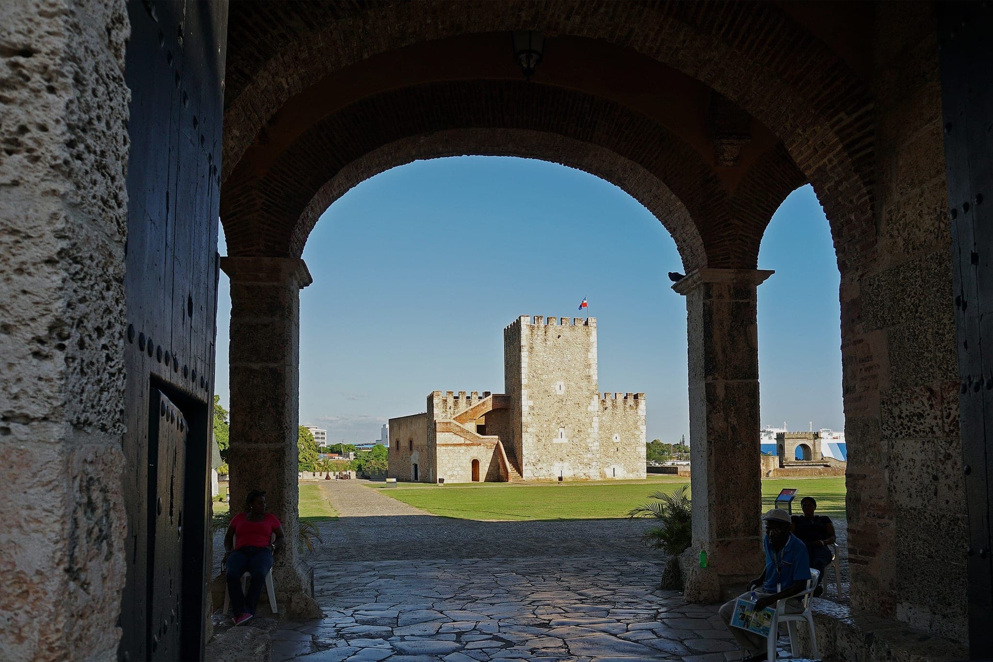 The Torre del Homenaje of the Fortaleza Ozama in Santo Domingo, seen through the stone gateway arch of the fort, under a blue sky.