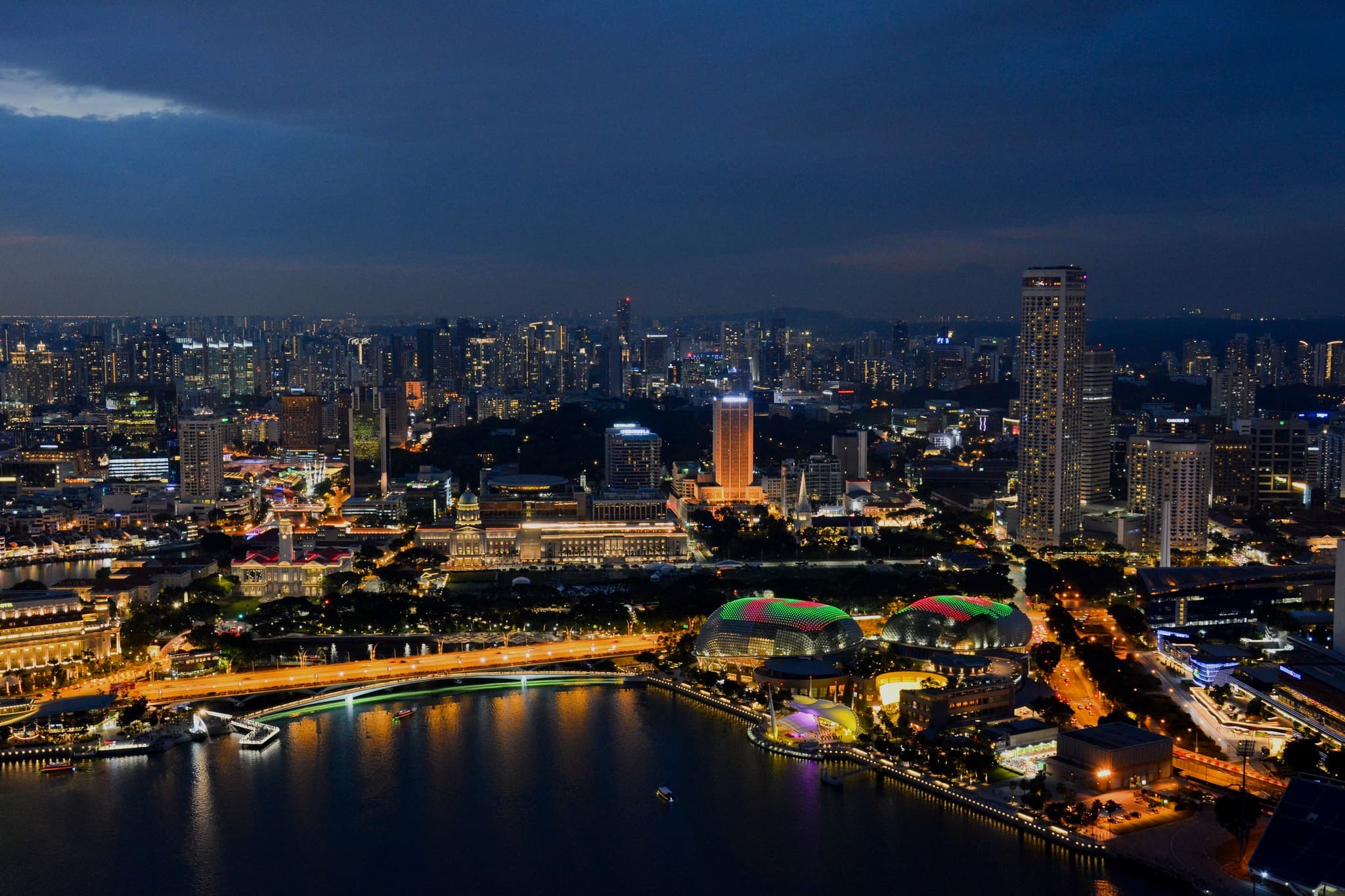 Marina Bay in Singapore at dusk, seen from above: the two spiky domes of the Esplanade theatre on the water, the lit bridges and the skyscrapers of the city centre behind them.