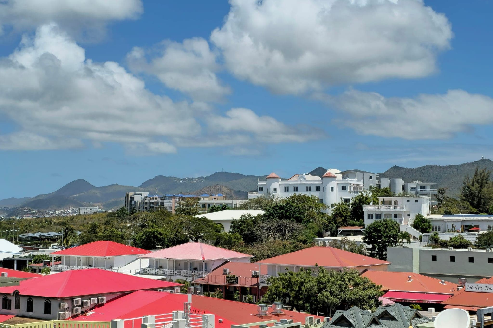 Sint Maarten seen from Maho: red and white roofs against the island's hills, under cumulus clouds.