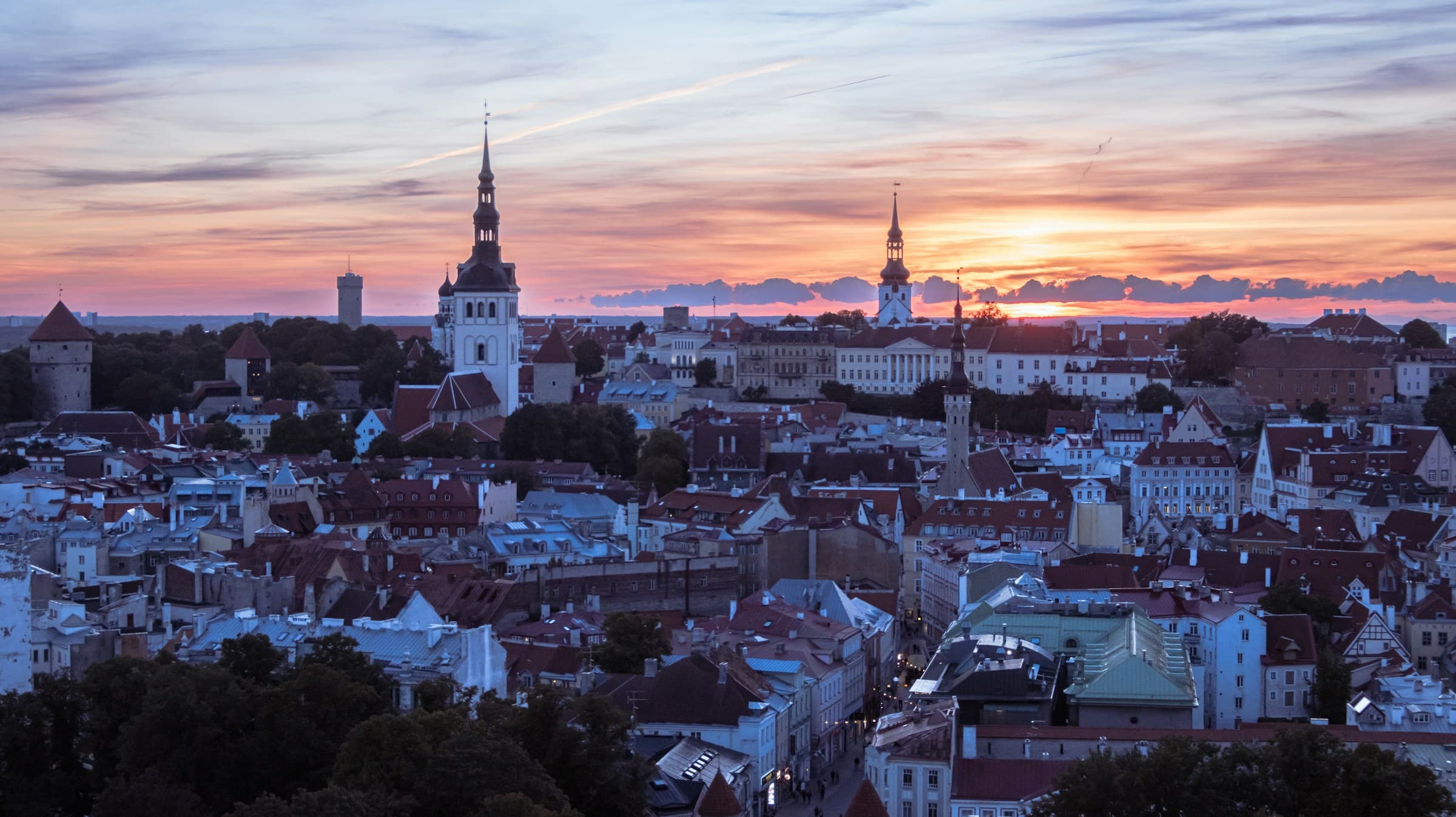 De oude stad van Tallinn bij zonsondergang, gezien vanaf de heuvel: de torens en spitsen boven de daken, met de laagstaande zon erachter.