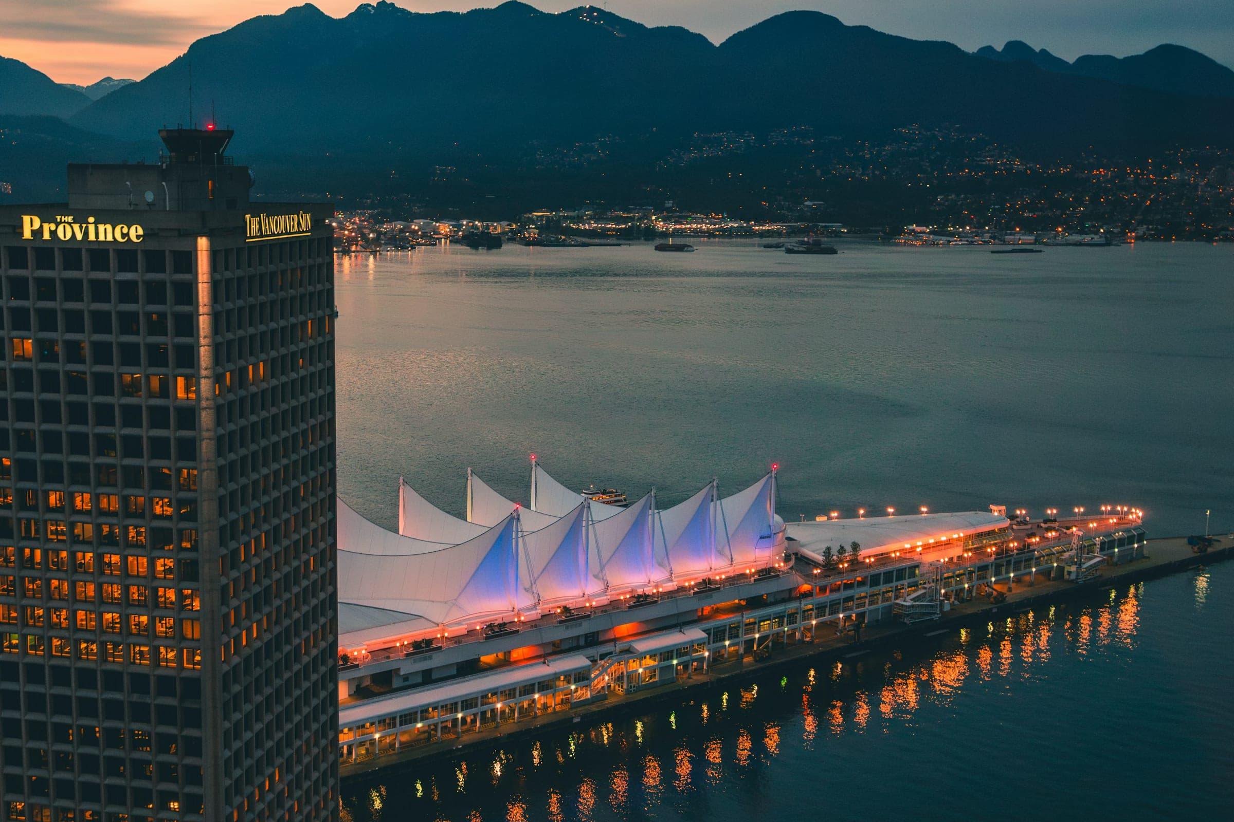 Canada Place aan de haven van Vancouver bij schemer, met de bergen van North Vancouver erachter.