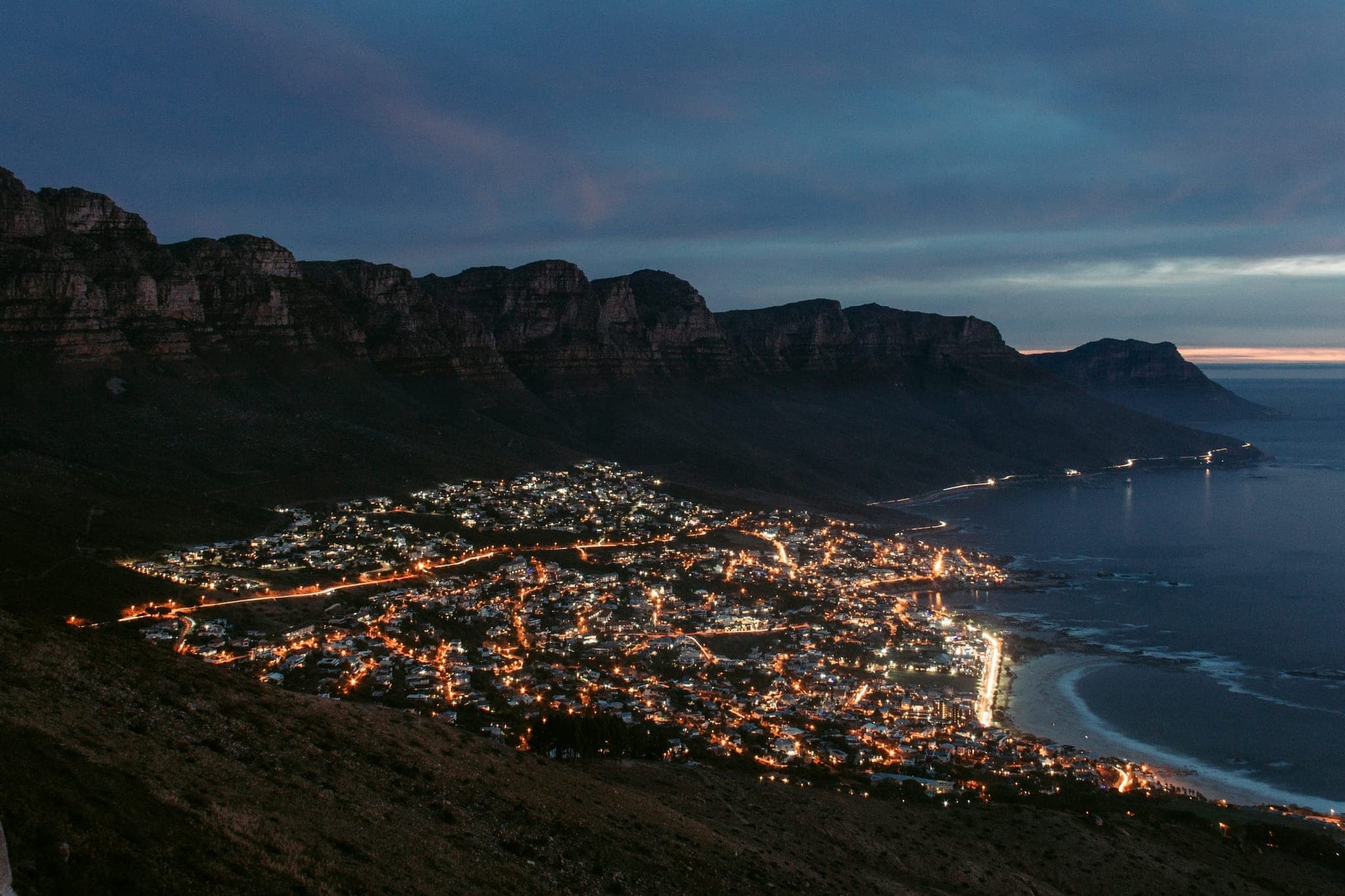 Camps Bay near Cape Town in the dark, from above: the cliffs of the Twelve Apostles above the lit bay.